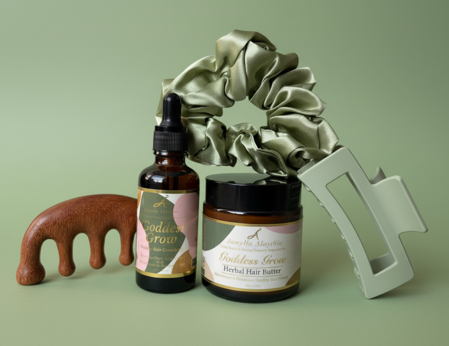Set of hair care products including an amber glass bottle os Goddess Grow Hair Growth Oil , an amber glass jar of Goddess Grow Herbal Hair Butter, a woden sandalwood comb, a sage green satin crunchie and sage green claw clip a on a sage green background