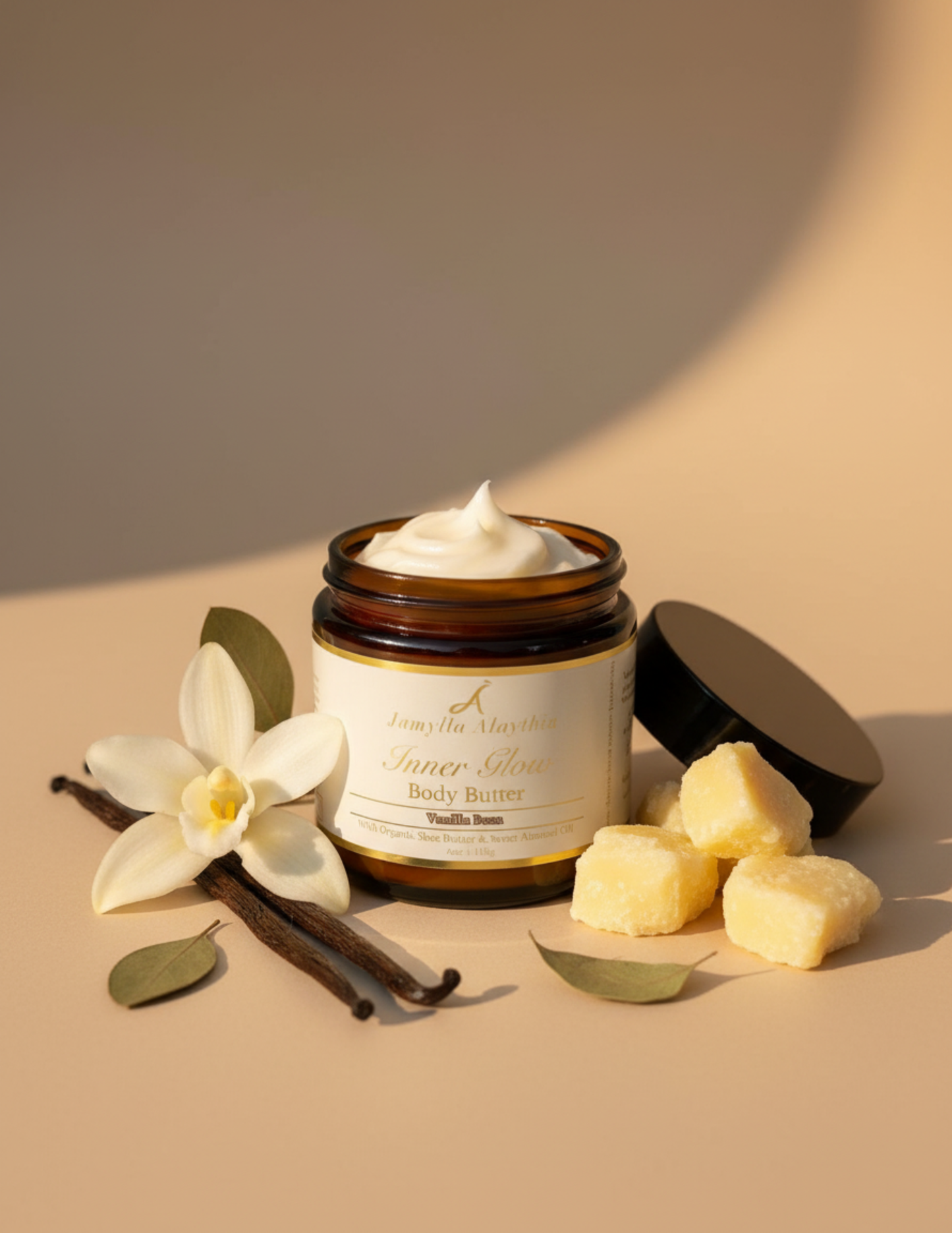 Amber glass Jar of body butter with cream label & vanilla flowers and vanilla beans &s shea butter around the jar on a beige background