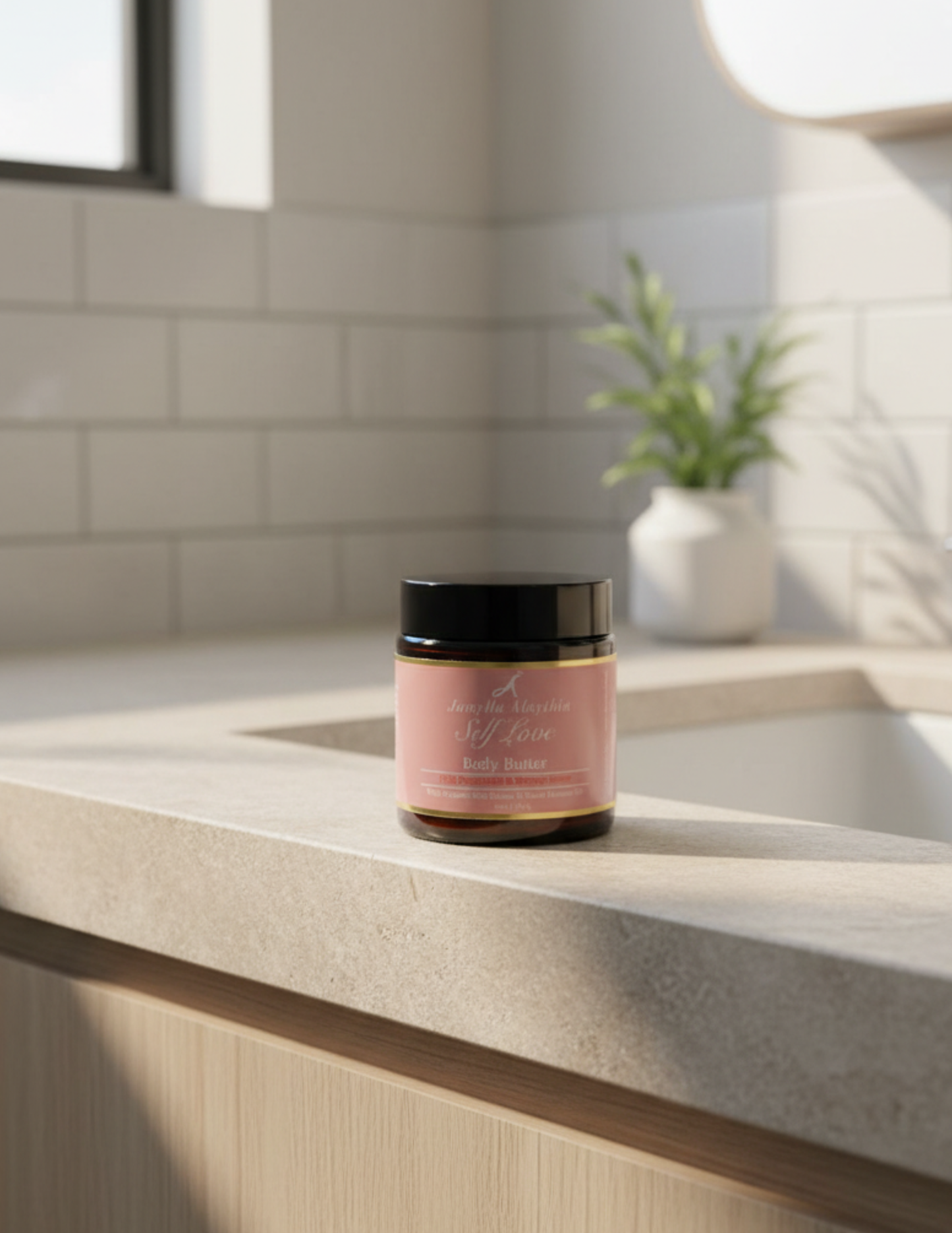 Amber glass Jar with pink label of self love body butter on a bathroom counter with a plant in the background