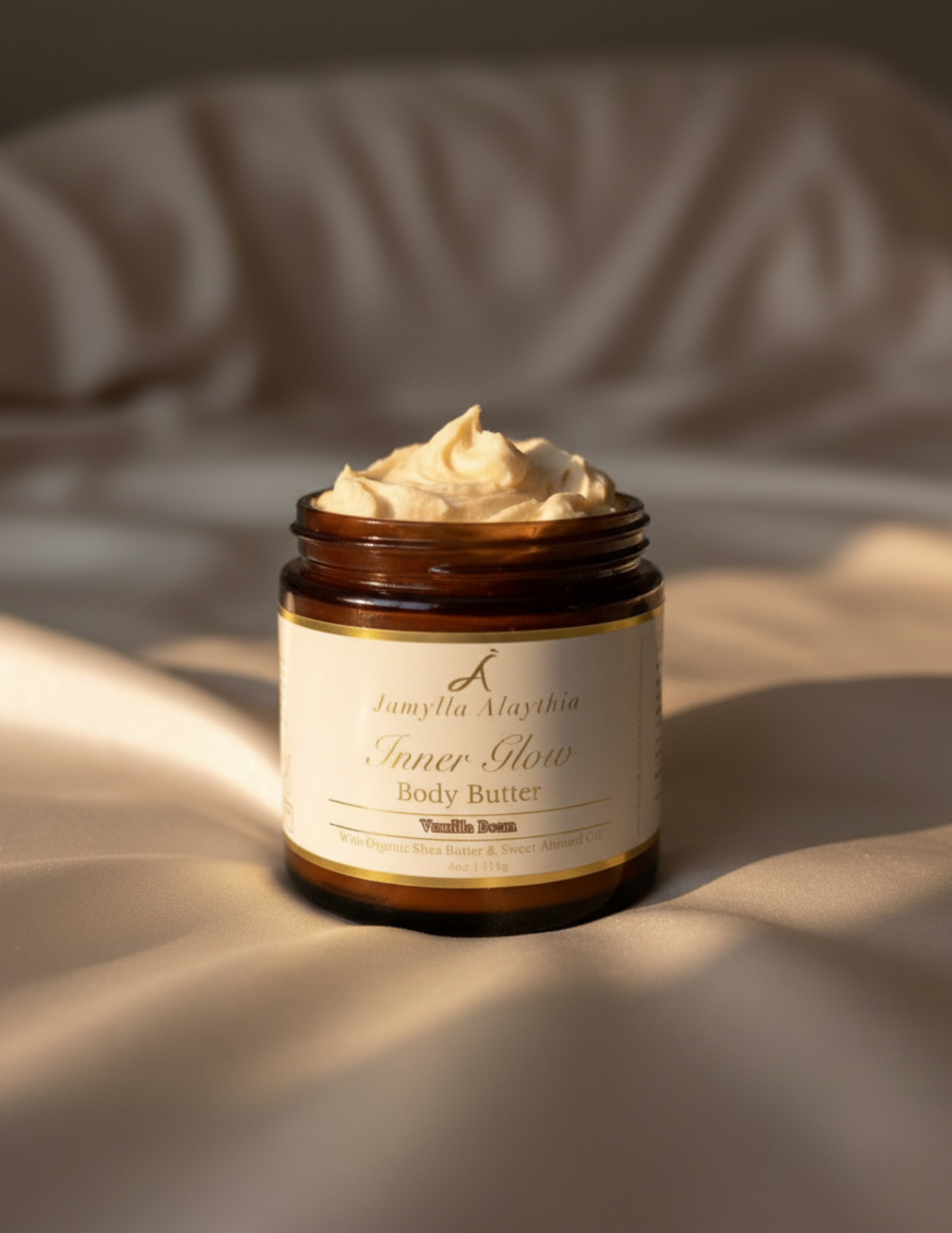 Jar of body butter, lid off showing whipped vanlila butter with a label on a soft, neutral background