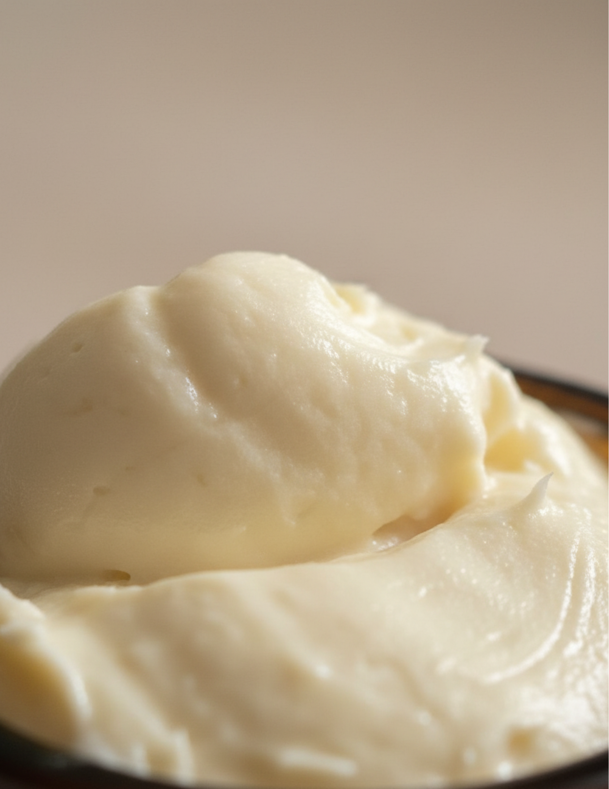 Close-up of whipped creamy body butter that looks like a scoop of vanilla ice cream on a plain background