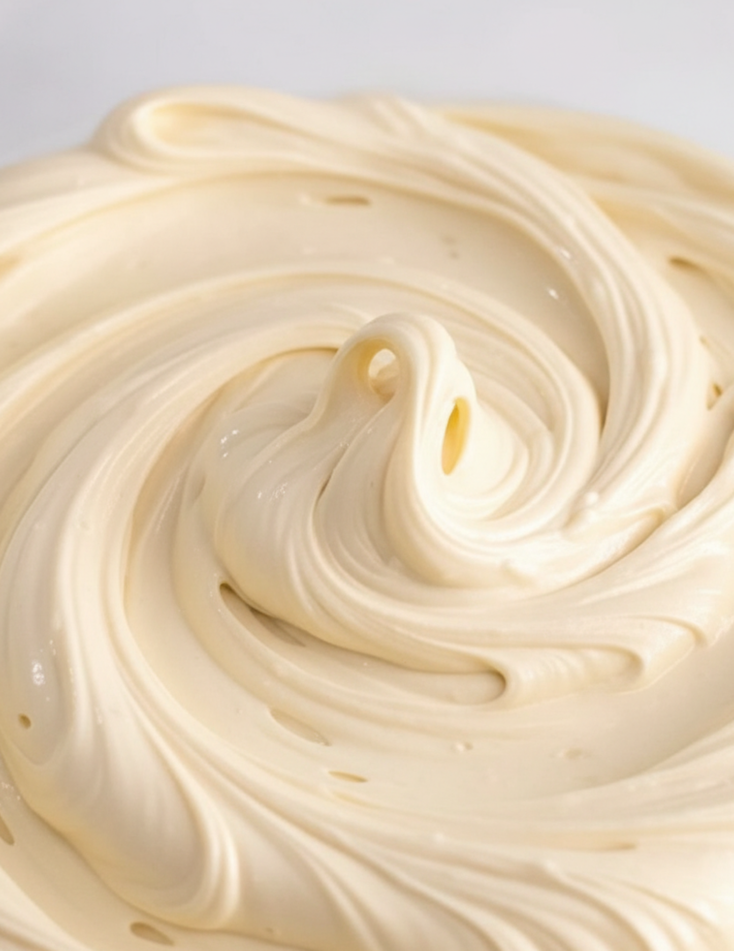 Close-up of creamy beige whipped body butter with a swirl pattern on a light gray background