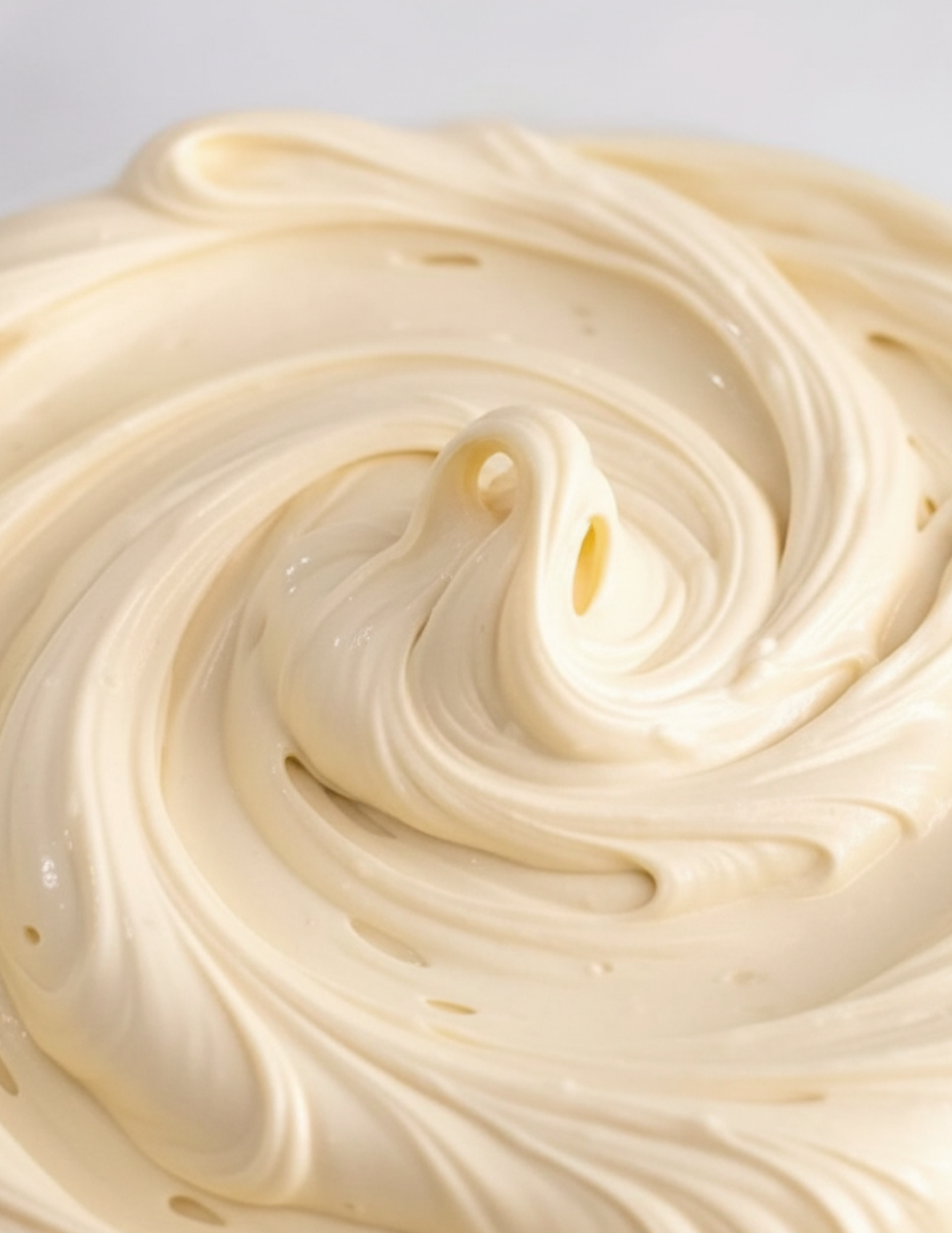Close-up of creamy beige whipped body butter with a swirl pattern on a light gray background