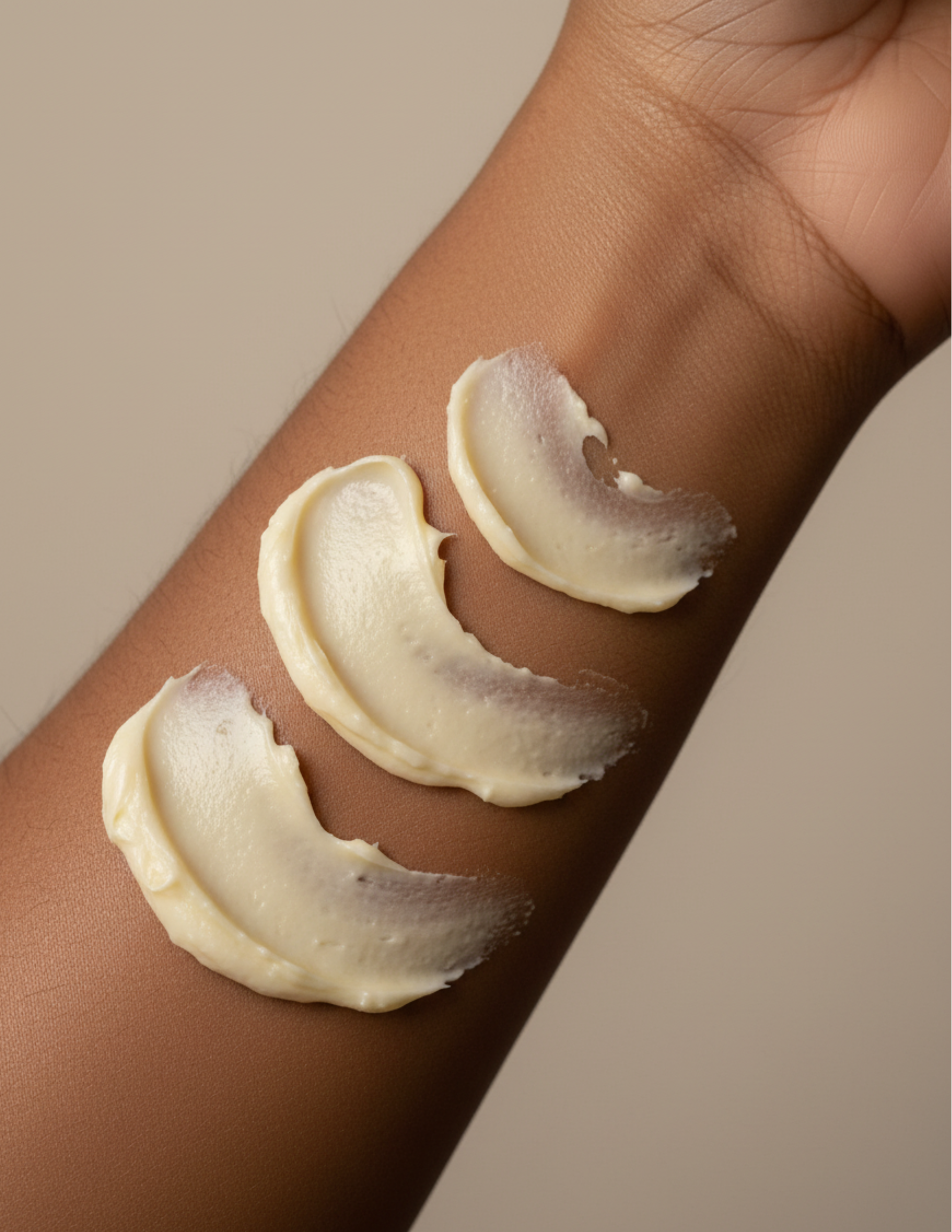 Three swatches of creamy whipped body butter on a person's arm that has glowy brown skin with a neutral background