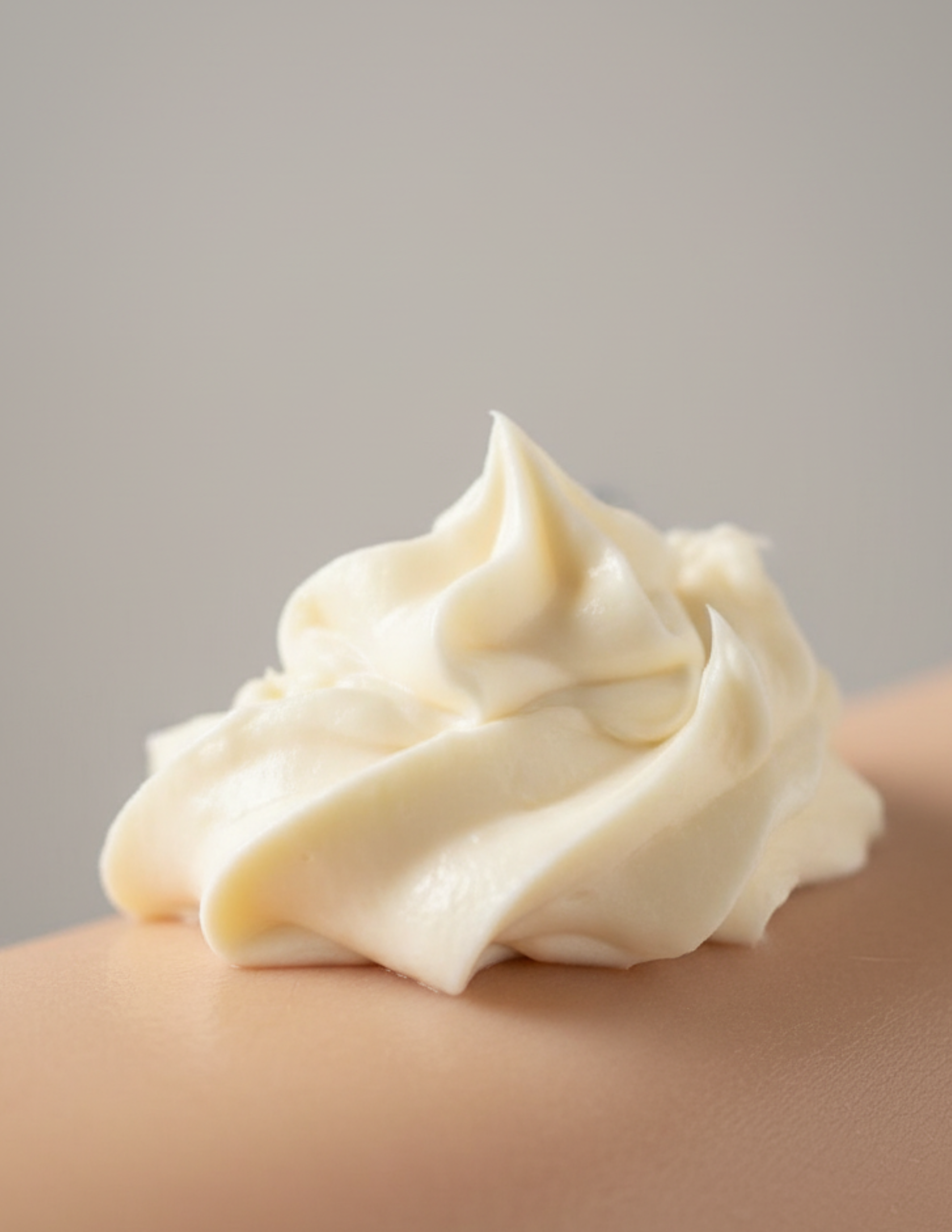 Creamy white creamy whipped body butter on a person's skin against a neutral background