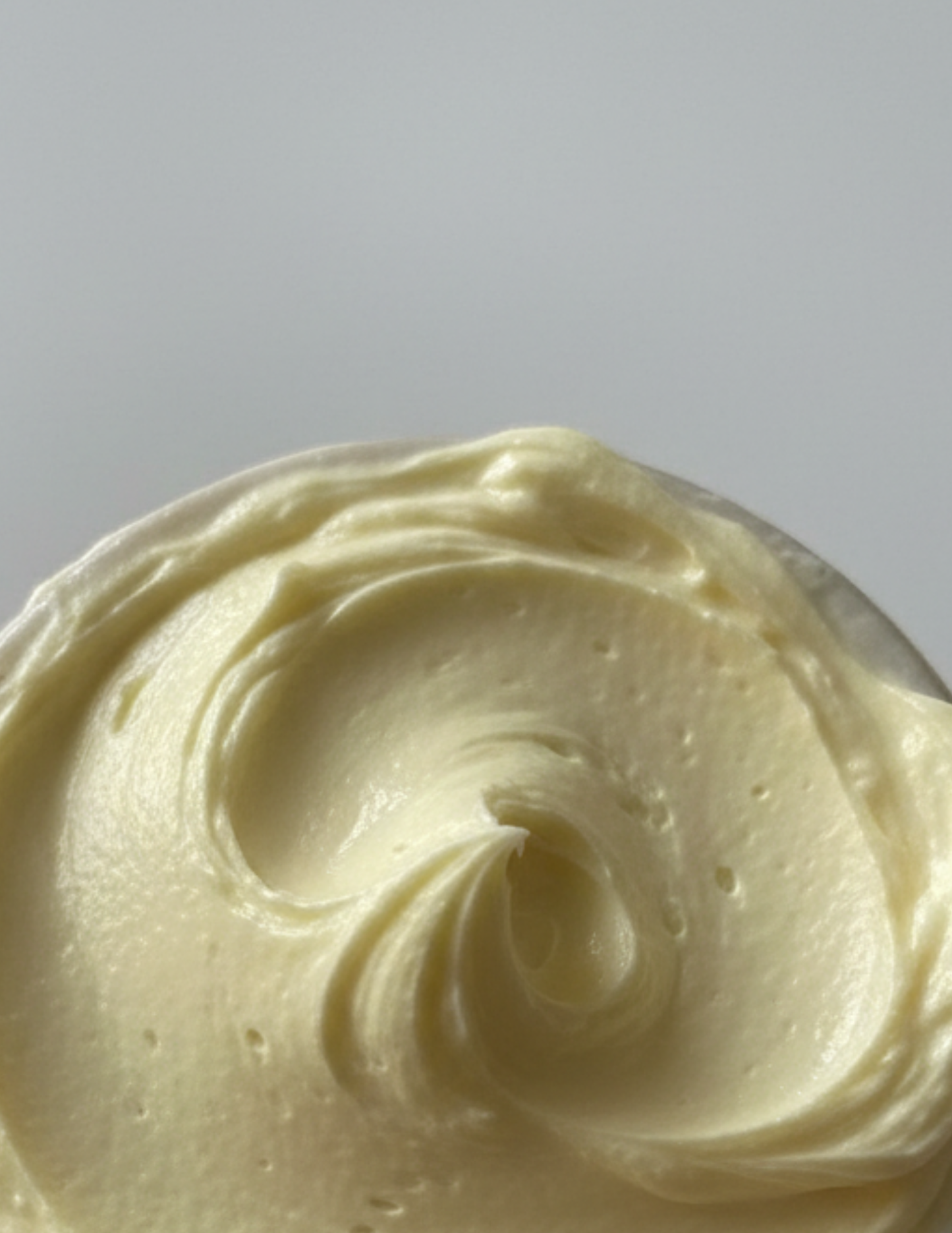 Close-up of creamy yellow hair and body butter on a gray background